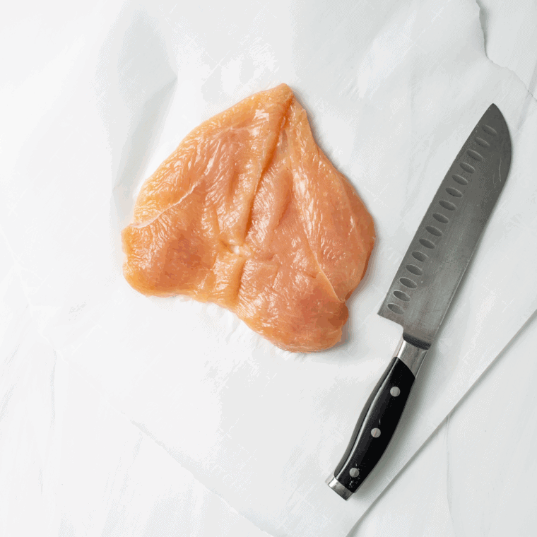 Butterflying a chicken breast with a sharp knife to create a pocket for stuffing.
