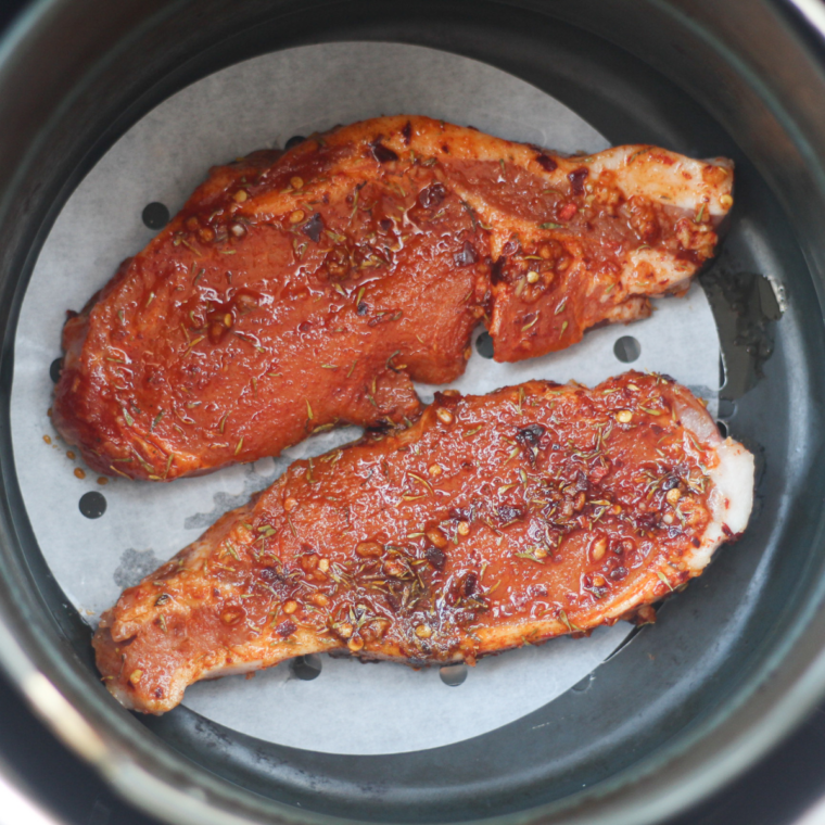 Pork steaks cooking in the air fryer basket, flipped halfway
