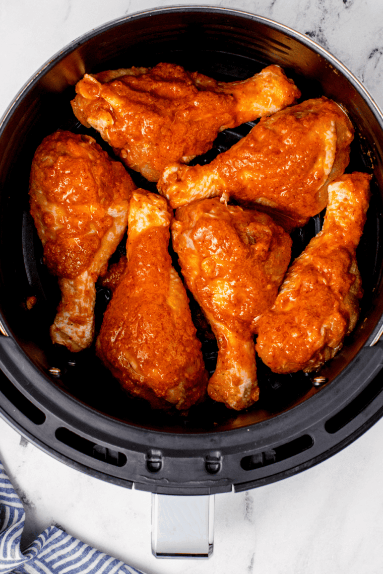 Buffalo chicken drumsticks arranged in air fryer basket in a single layer cooking until golden brown and crispy