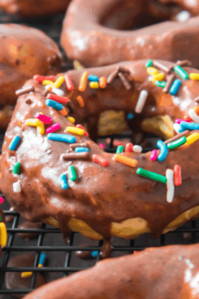 Freshly air-fried chocolate glazed donuts stacked on a plate with extra glaze drizzle.