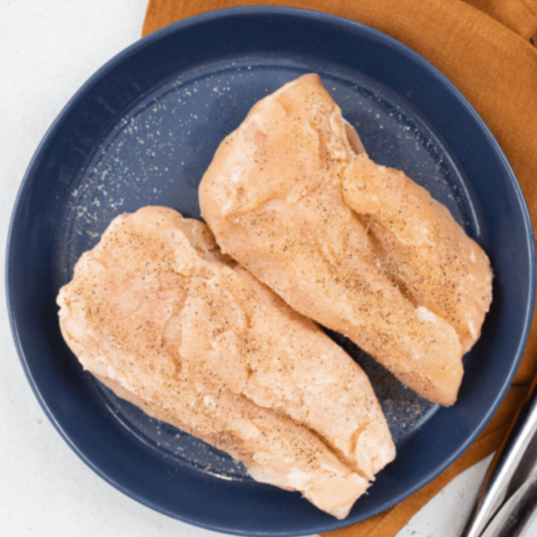 A hand coating a chicken breast in a mixture of panko breadcrumbs and ground pecans before air frying.