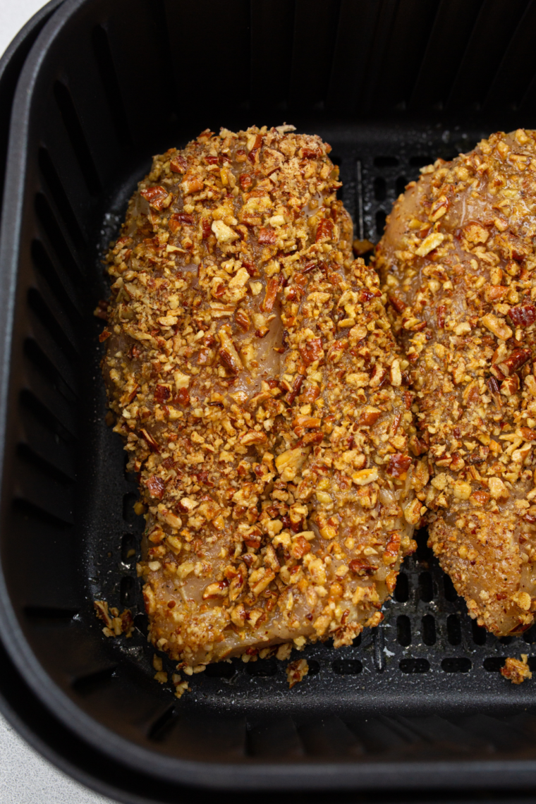 "The air fryer basket loaded with pecan-crusted chicken breasts, ready to be cooked."