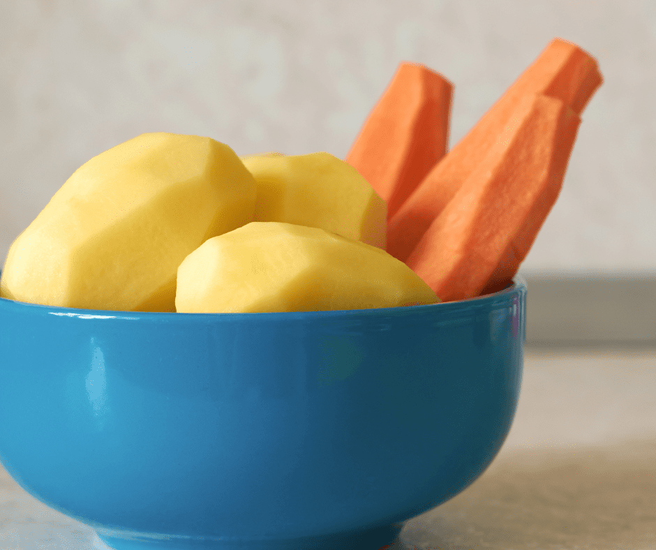 Ingredients needed for this recipe. 3 peeled carrots and 3 peeled potatoes are sitting in a bright blue bowl in a white kitchen.