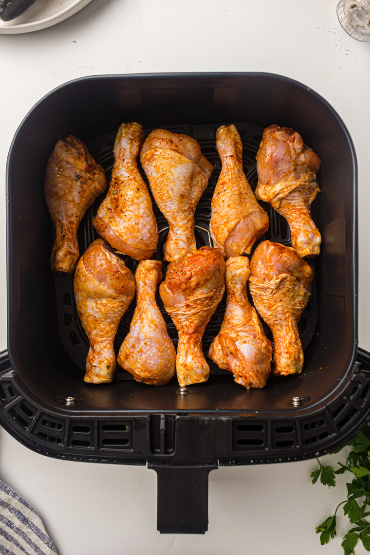 Seasoned chicken drumsticks in a single layer in an air fryer basket