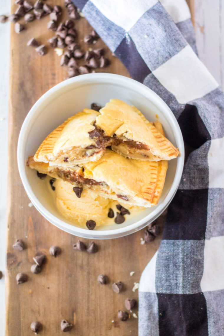 Air Fryer S'mores Hand Pies served with a side of chocolate dipping sauce and fresh berries on a rustic wooden table.