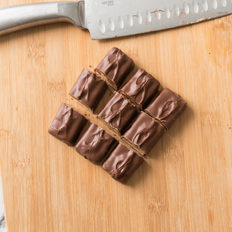 Unwrapped Snickers bars cut into thirds and placed on biscuit dough rounds, ready to be wrapped.