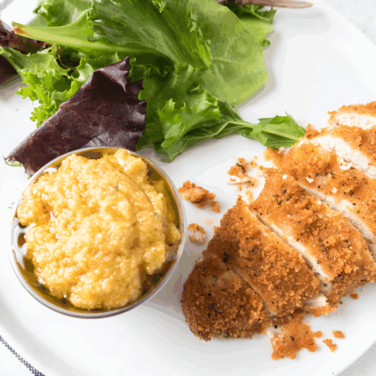 Crispy Parmesan crusted chicken topped with fresh arugula and lemon vinaigrette, served on a white plate.