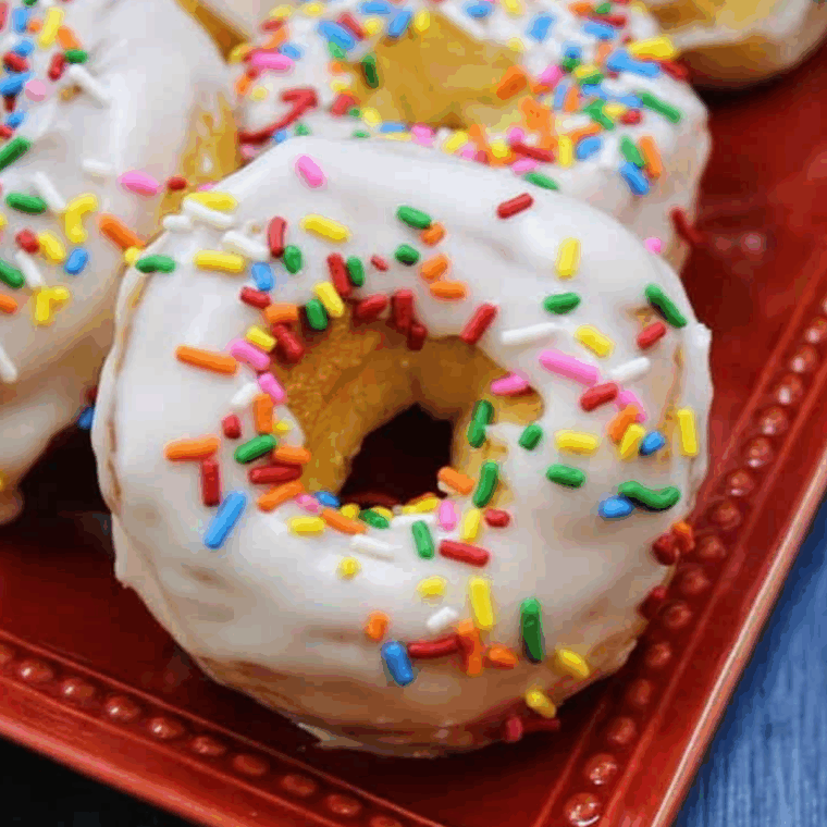Freshly baked Dunkin’ Donuts sprinkle donuts with glaze and rainbow sprinkles on a plate.