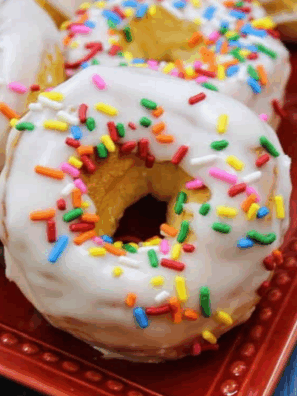 Homemade Dunkin’ Donuts sprinkle donuts topped with glaze and rainbow sprinkles on a cooling rack.