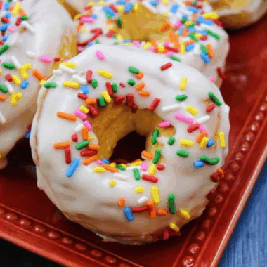 Homemade Dunkin’ Donuts sprinkle donuts topped with glaze and rainbow sprinkles on a cooling rack.