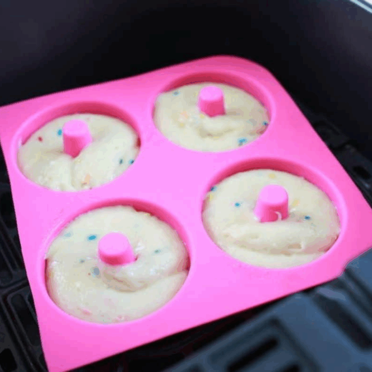 Pouring donut batter into silicone molds and air frying at 320°F before cooling and frosting.