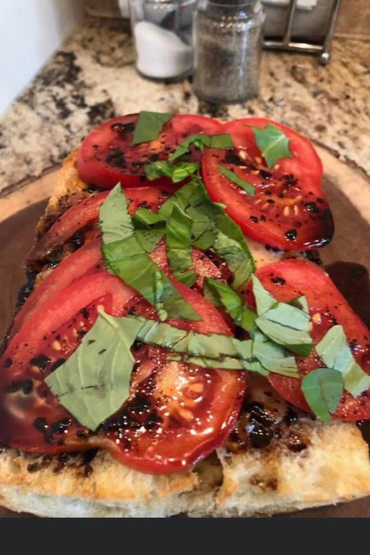 Caprese garlic bread served as an appetizer with fresh basil and a bowl of balsamic glaze