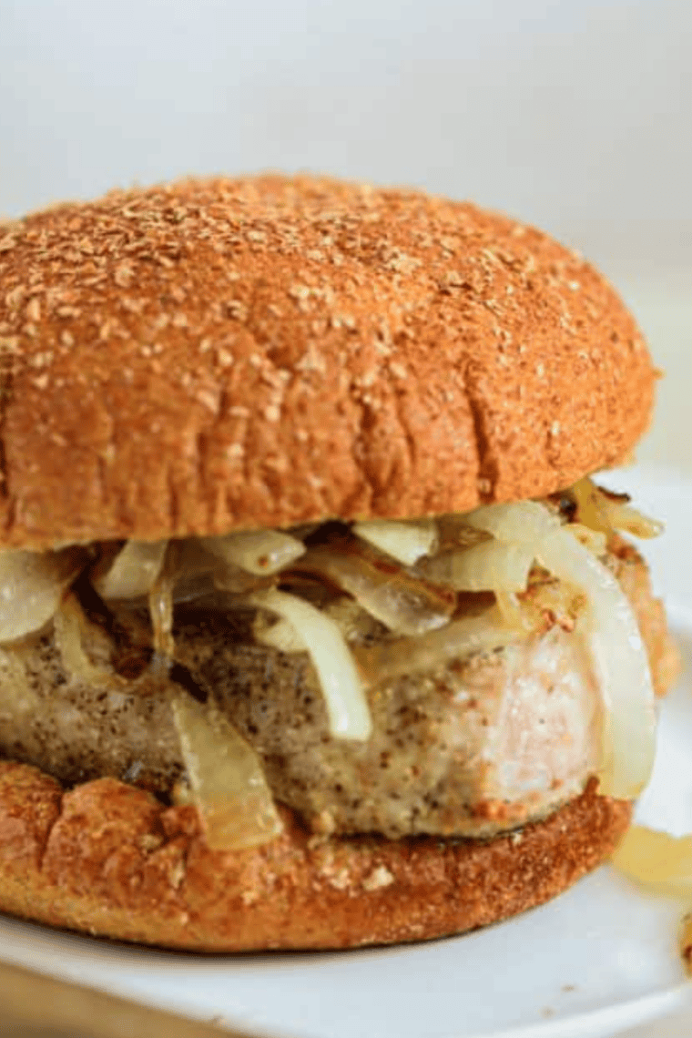 Two air fryer pork chop sandwiches stacked, topped with saut&eacute;ed onions on hamburger buns