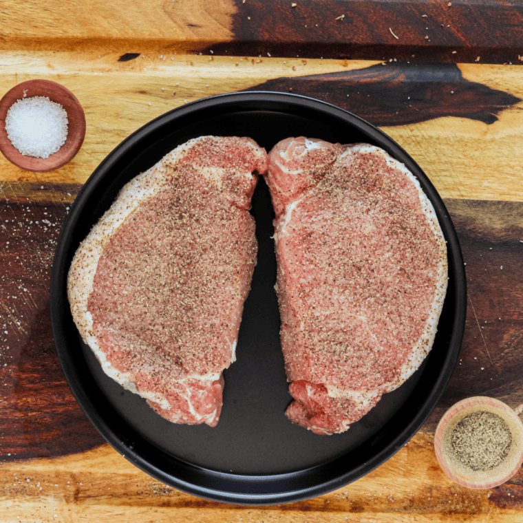 Seasoned pork chops arranged on a black plate.