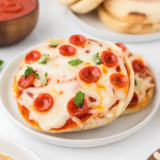 Air fryer English muffin pizzas topped with melted cheese and various toppings, cooked to crispy perfection in minutes."