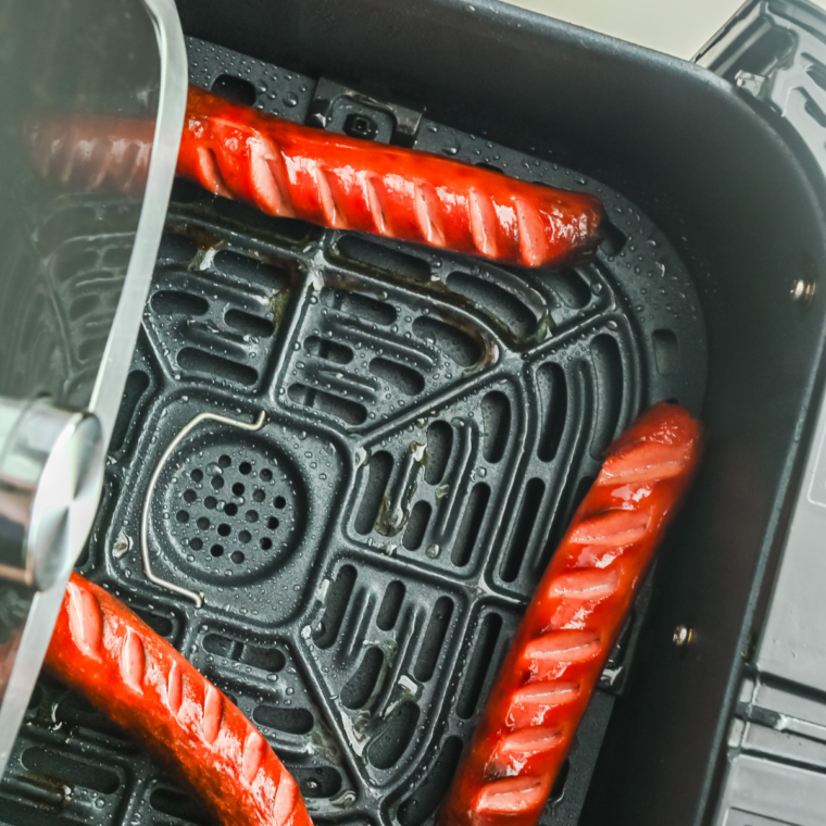 Hot dogs cooking in an air fryer basket with lightly crisped edges and juicy centers, ready to serve in buns.