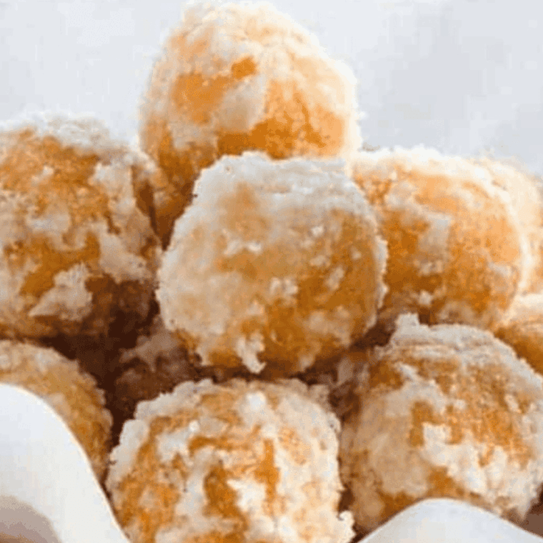 A pile of golden-brown air fryer zeppole dusted with a thick layer of snowy powdered sugar on a white serving platter.