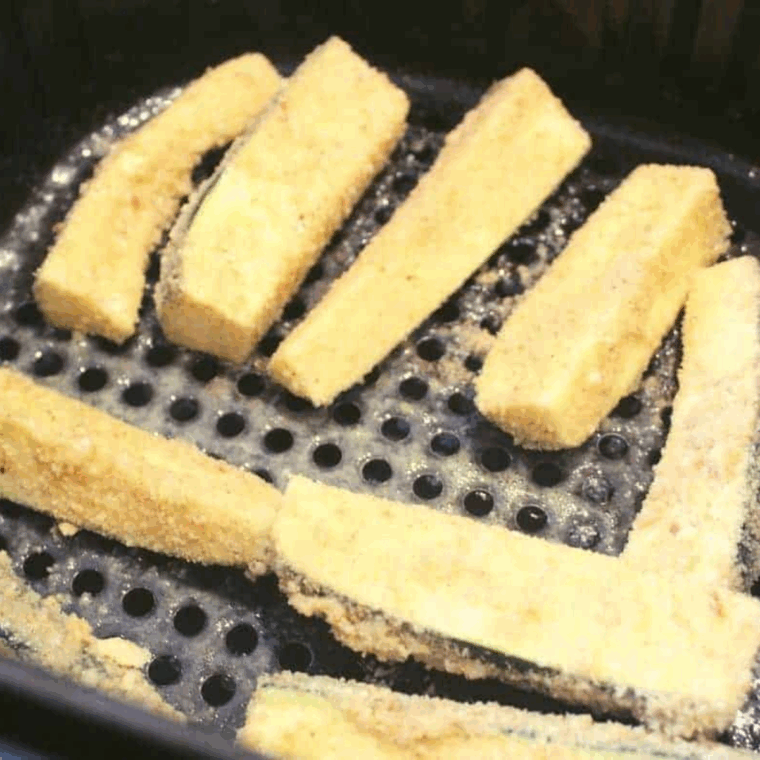 Place breaded zucchini fries into the air fryer basket, spray with cooking spray, and cook at 370°F for 7 minutes, flip, spray again, and cook an additional 7 minutes until golden brown.