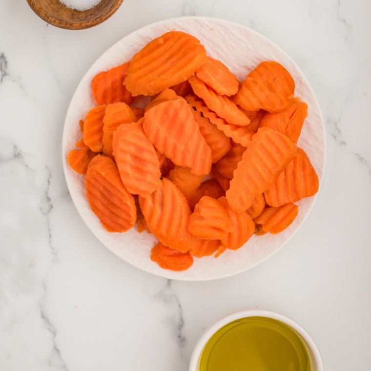 Ingredients needed for carrot chips on a white table.