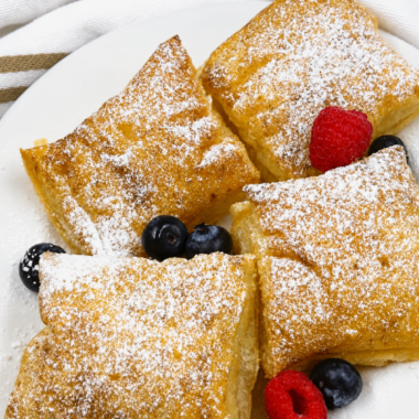 Air fryer puff pastry French toast squares dusted with powdered sugar and topped with fresh berries