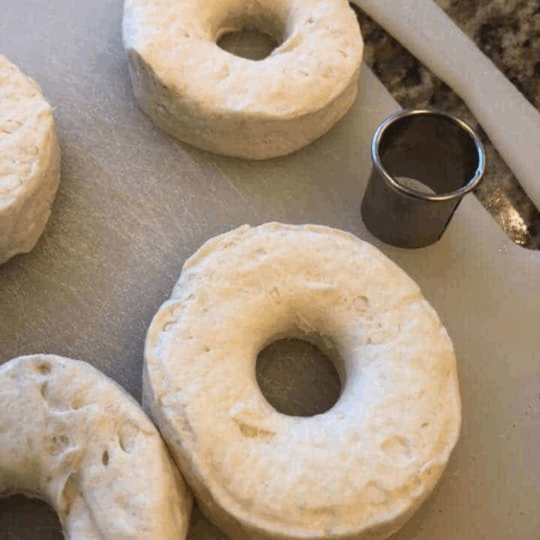 Opening biscuit can, cutting centers to form donuts and donut holes, and brushing with melted butter for flavor.