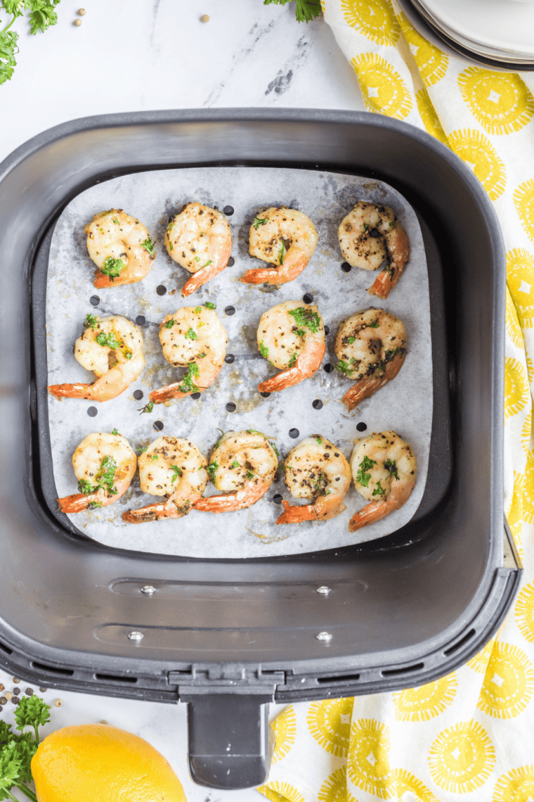 Golden-brown colossal garlic shrimp in an air fryer, garnished with parsley and lemon slices.