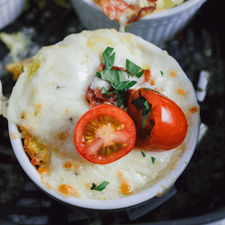 Air fryer spinach and tomato frittata in ramekins topped with melted cheese, crispy bacon, and grape tomato halves, ready to serve.