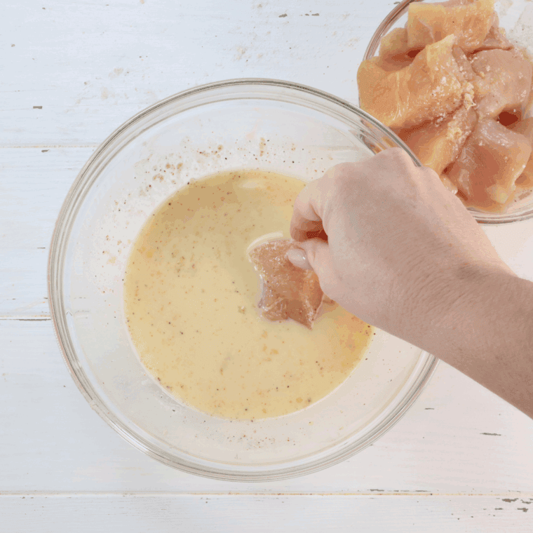 Chicken pieces being dipped in egg mixture.