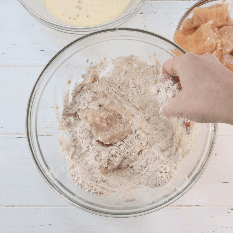 Chicken pieces being coated with the flour mixture.