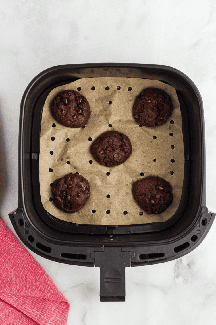 Scoop and roll tablespoon-sized portions of Air Fryer Double Chocolate Chip Cookie dough into balls, placing them on parchment paper before air frying for 8-10 minutes until golden and set.