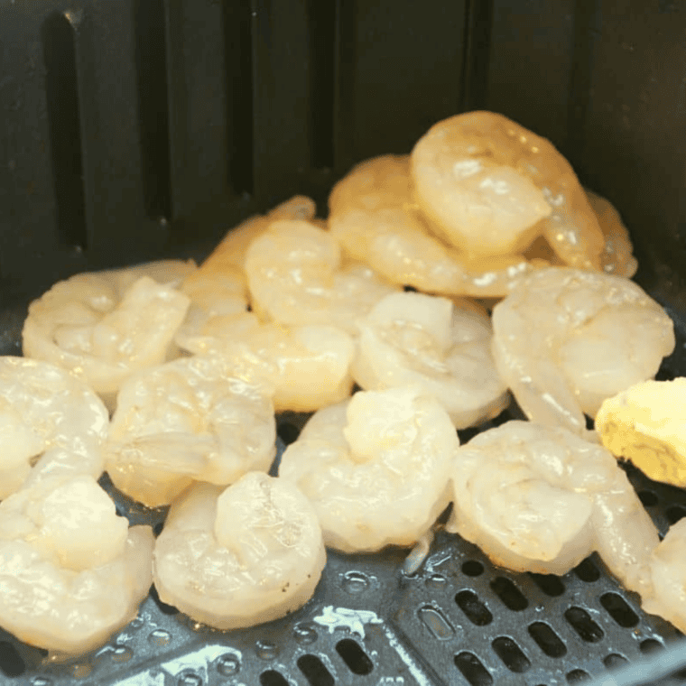 Shrimp arranged in an air fryer basket ready to cook at 400&deg;F, midway through flipping.