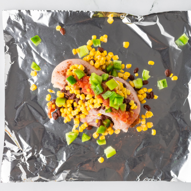 Step showing black beans and corn being added to the foil packet with the seasoned chicken.