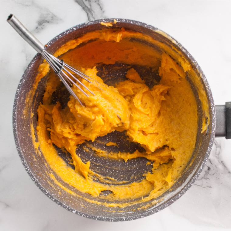 Mixing bowl with pumpkin pie filling ingredients being combined, showcasing a rich orange mixture.