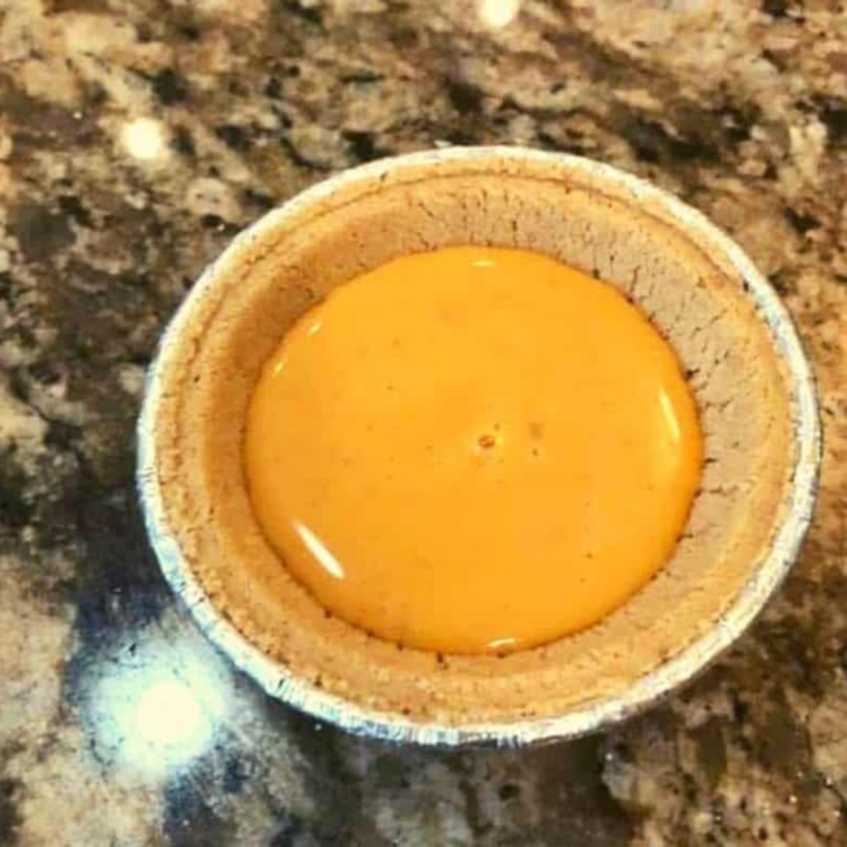 Image of pouring filling into crust: "Pouring the pumpkin pie filling into a graham cracker crust in preparation for air frying."