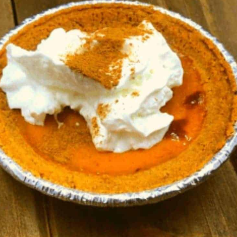 A freshly baked Air Fryer Pumpkin Pie with a golden graham cracker crust, topped with whipped cream and a sprinkle of cinnamon, served on a rustic wooden table.