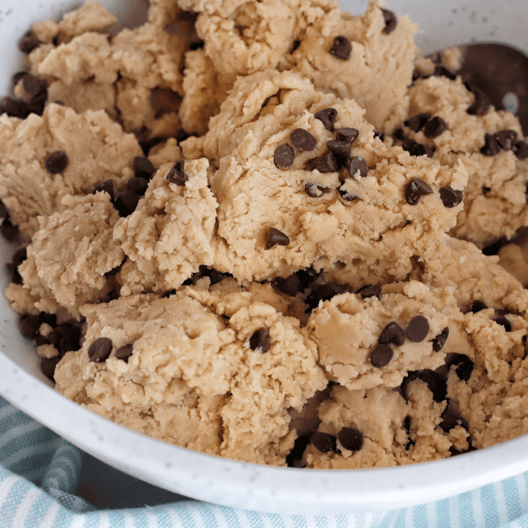 Chocolate chips and raisins being folded into oatmeal cookie dough in a mixing bowl.