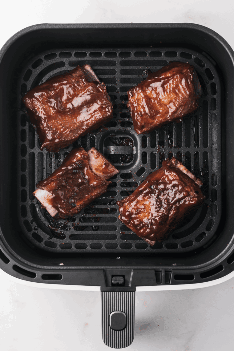 Marinated Korean short ribs cooking in a single layer in the air fryer basket with caramelized, crispy edg