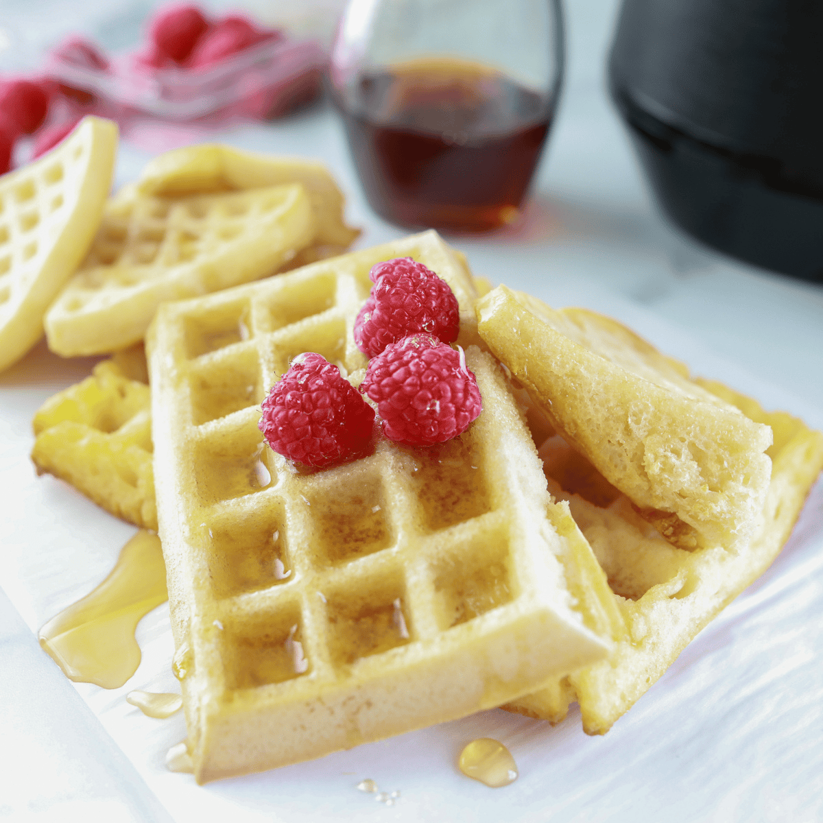 Golden homemade waffles cooked in the air fryer, stacked on a plate with butter and maple syrup.