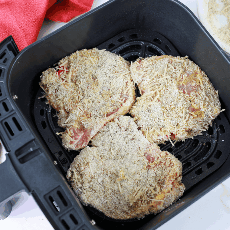 Cooking coated pork chops in air fryer, flipping halfway through.