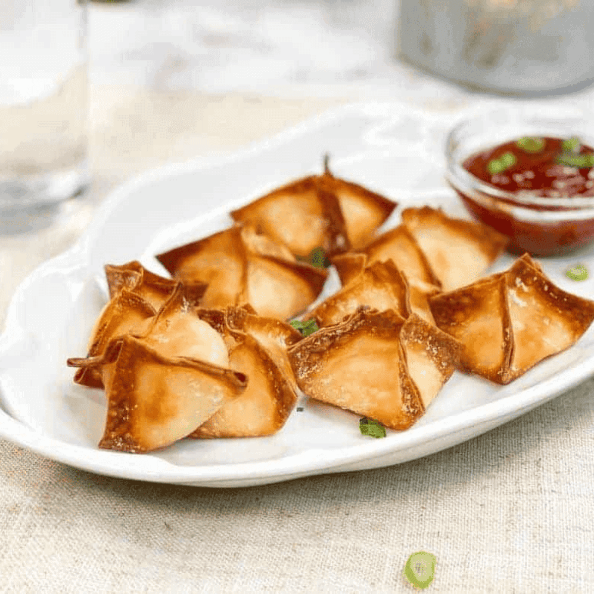 Golden P.F. Chang’s style crab rangoons filled with cream cheese and crab meat on a serving plate with dipping sauce.