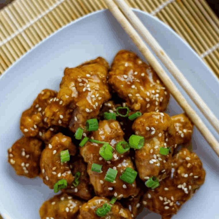 Crispy sweet and sour chicken coated in a glossy tangy sauce on a white plate.