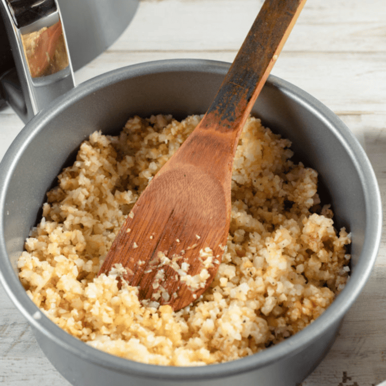 Cooking cauliflower rice mixture in an air fryer pan, then adding beaten eggs and air frying until set and cooked through