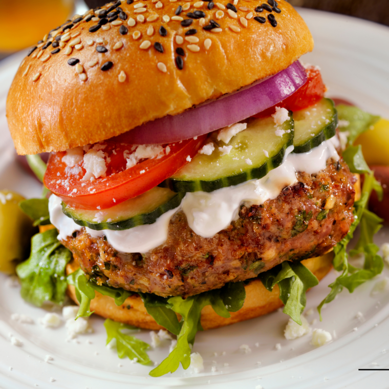 "Air Fryer Greek Burger on a bun with fresh veggies and a dollop of tzatziki."