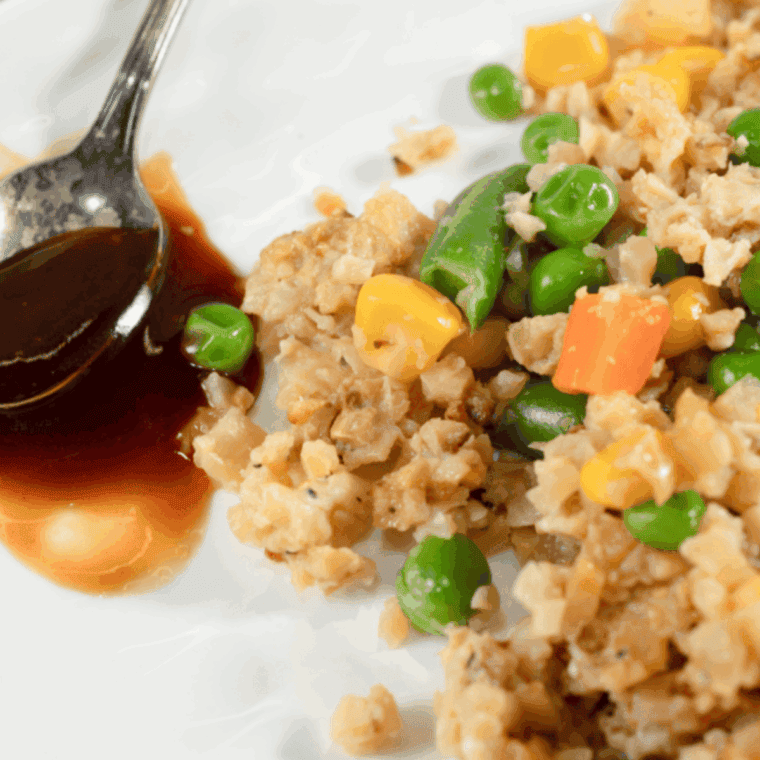 Benihana-style garlic chicken cauliflower fried rice served on a plate with green onions and colorful vegetables.