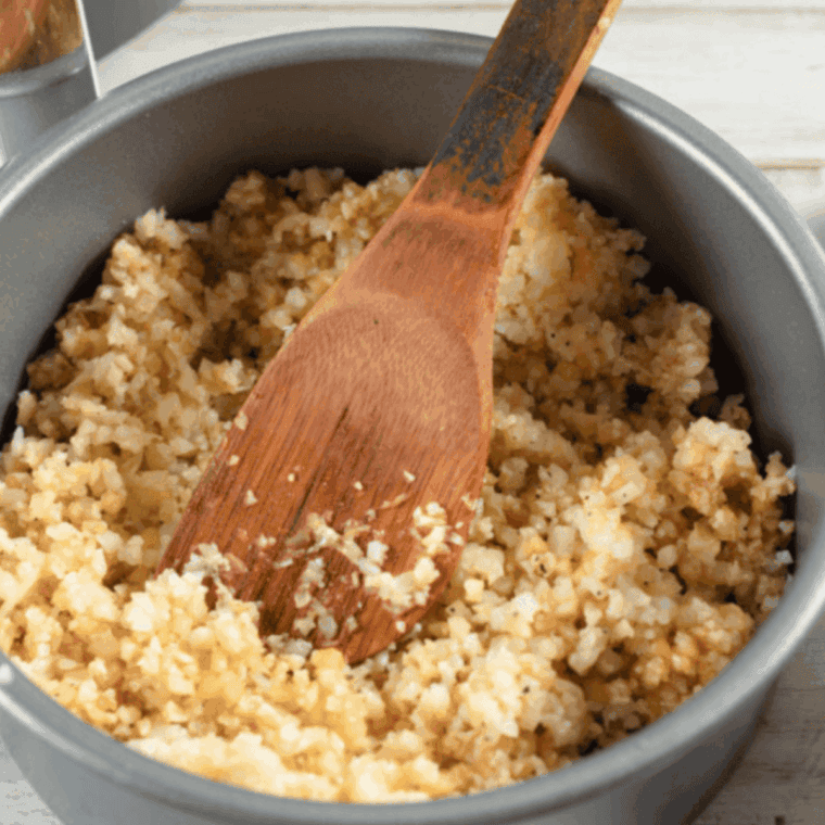 Cooking cauliflower rice mixture in an air fryer pan, then adding beaten eggs and air frying until set and cooked through
