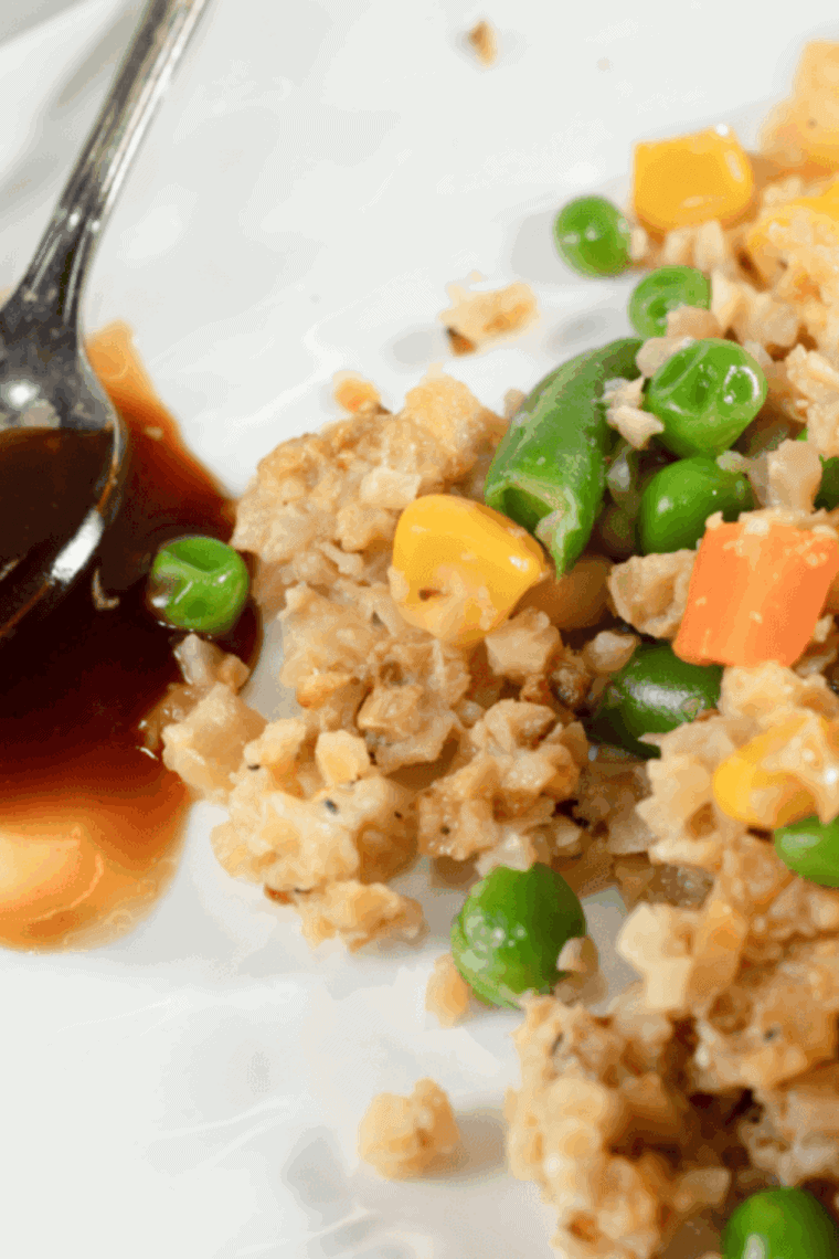 Plate of Benihana-style garlic chicken cauliflower fried rice garnished with green onions and colorful vegetables.