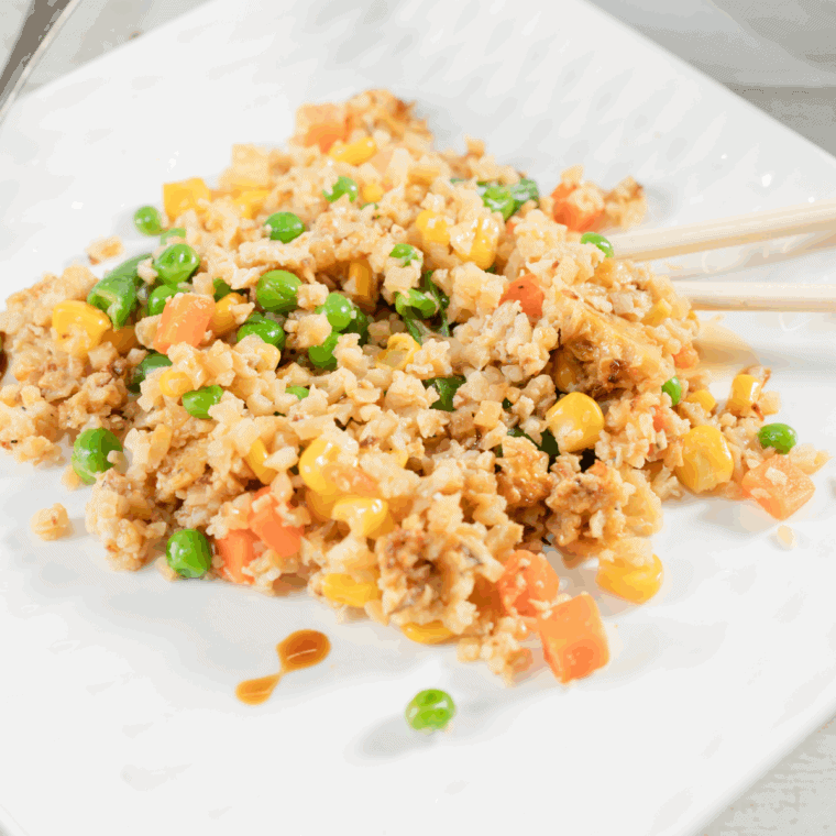 Benihana-style garlic chicken cauliflower fried rice served on a plate with green onions and colorful vegetables.