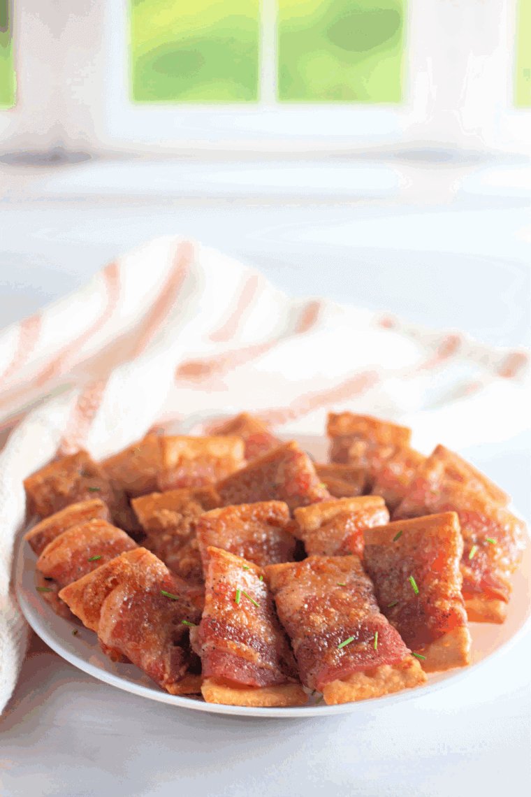 Golden-brown bacon wrapped around crunchy crackers, served on a small plate, ready to enjoy as a tasty air fryer snack.