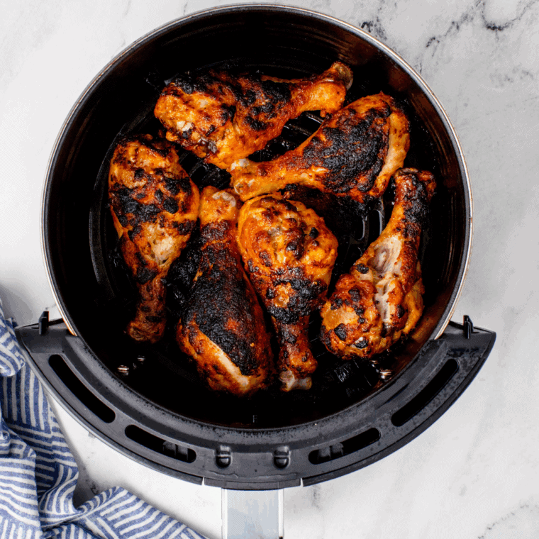 Air fryer Korean BBQ chicken drumsticks with sticky glaze, garnished with sesame seeds and green onions on a serving plate.