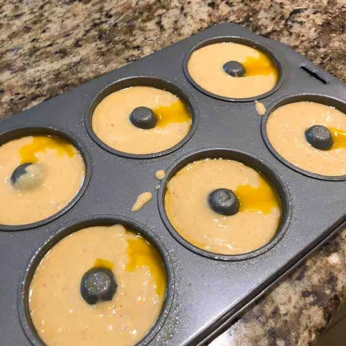 Filling an air fryer-safe donut pan or piping batter onto parchment paper to form donut shapes.